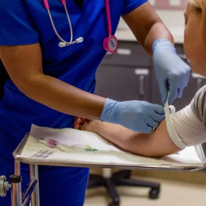 Healthcare worker in blue scrubs preparing a patient's arm for blood draw, applying a tourniquet in a medical clinic setting. Phlebotomy technician"