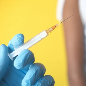 Close-up of a healthcare professional's gloved hand holding a syringe with a needle, preparing for injection administration.