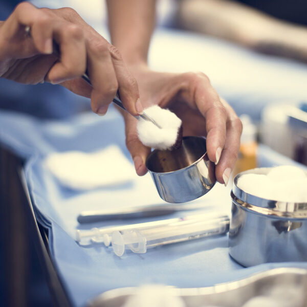 Close-up of medical professional using sterile forceps to pick up cotton ball from stainless steel container in surgical preparation setting