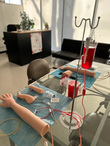 iv-simulation Phlebotomy training setup with IV arms, blood draw equipment, and medical supplies on a classroom table